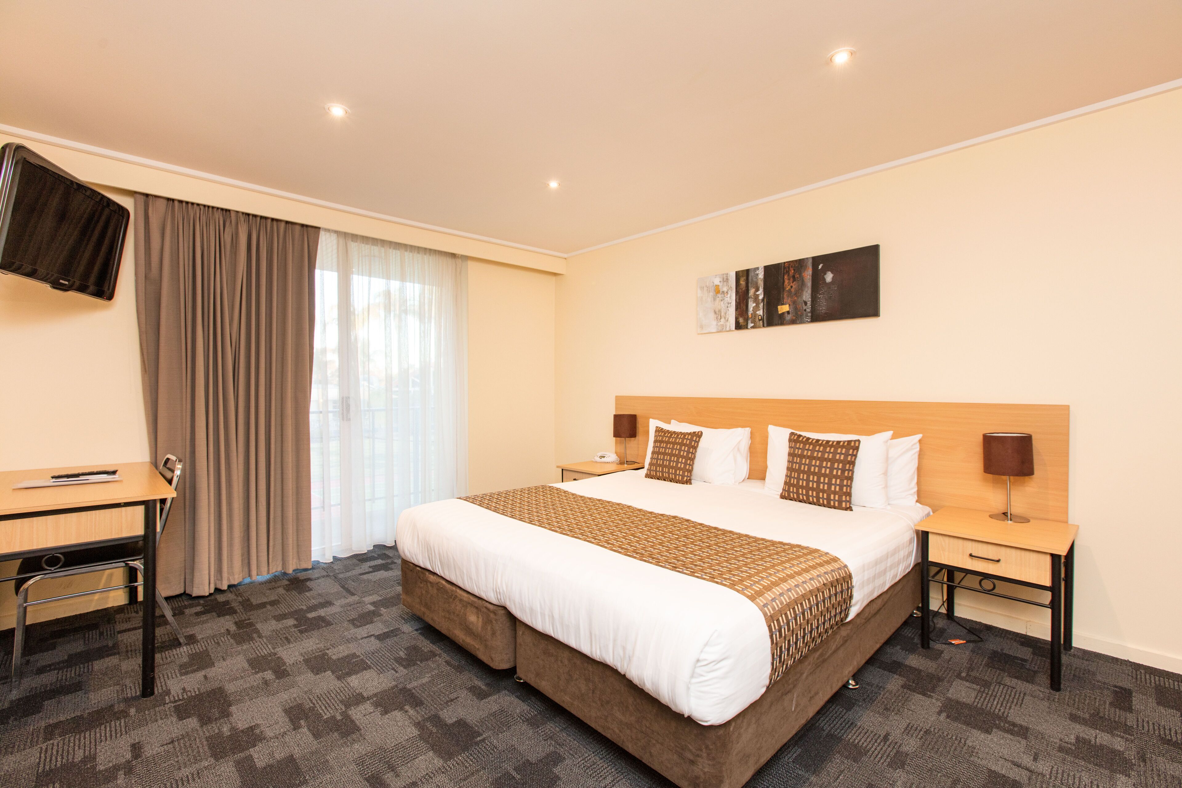 A hotel room with a large bed, a desk, a flat-screen TV, and a window with curtains.
