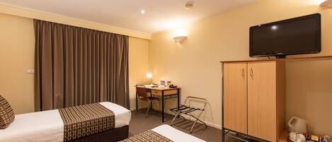 Een hotelkamer met twee bedden, een bureau, een televisie en een kledingkast.