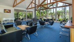 Un espacio interior amplio con techos altos, ventanas grandes y vista a palmeras.