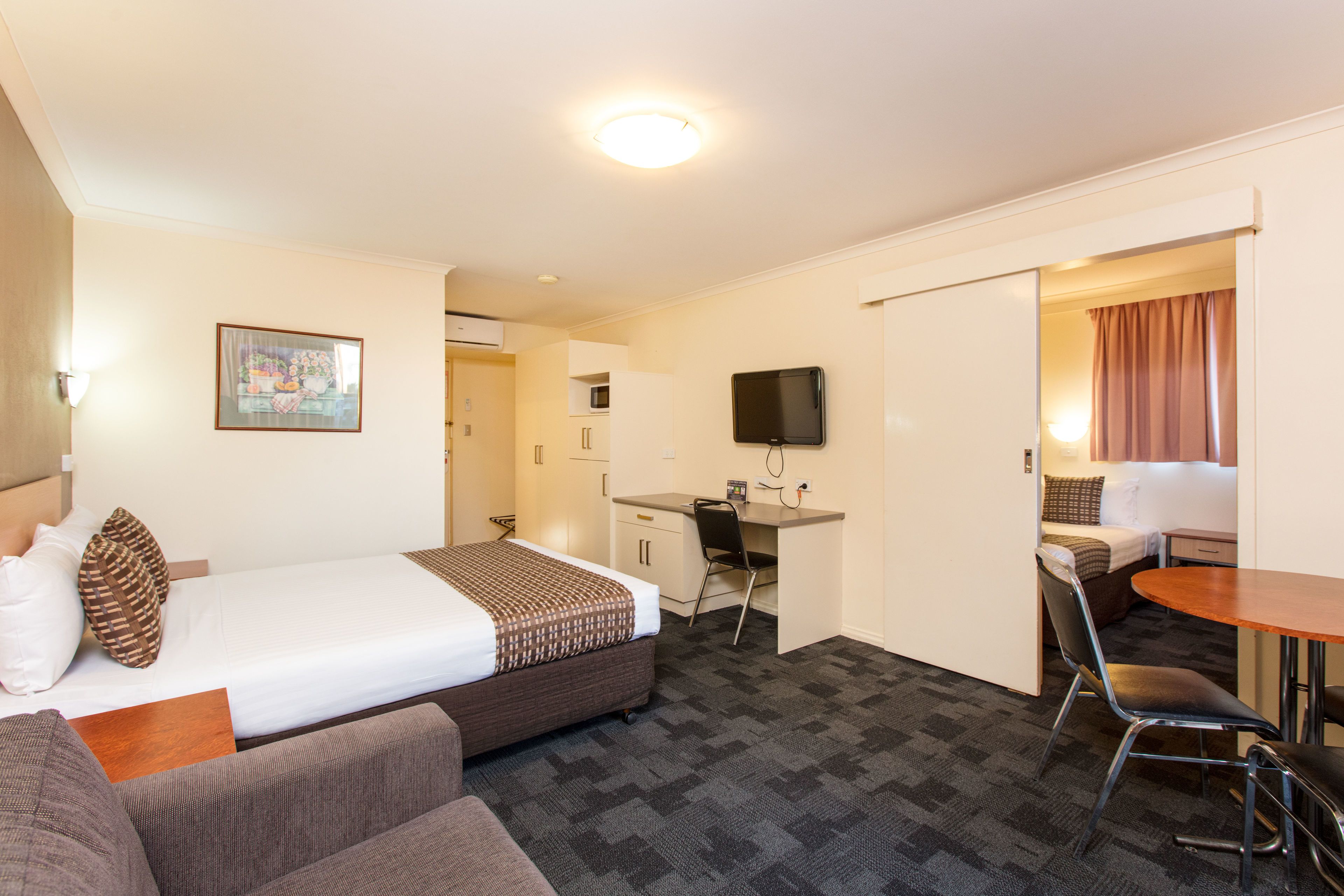 A hotel room with a bed, a desk, a chair, a television, and a small dining table.