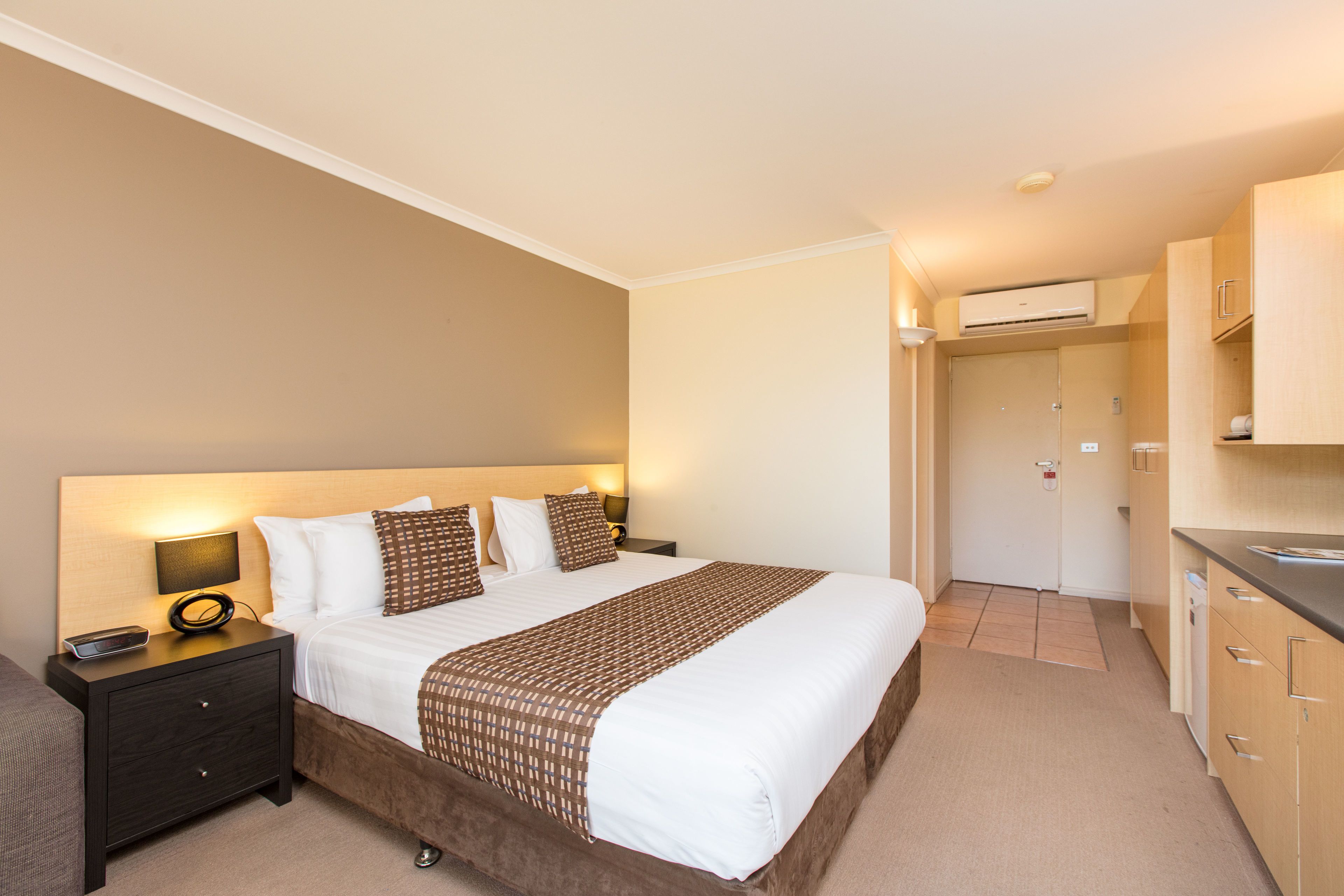 A hotel room with a large bed, bedside tables, a desk, and a kitchenette.