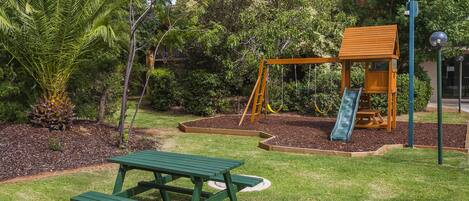 A playground with a swing set and slide, surrounded by trees and a picnic table.