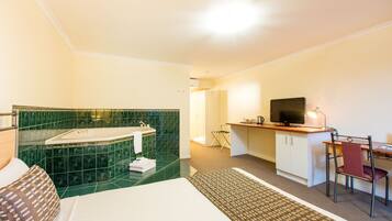 Una habitación de hotel con una cama, un escritorio con una silla, un televisor y un baño con bañera y azulejos verdes.