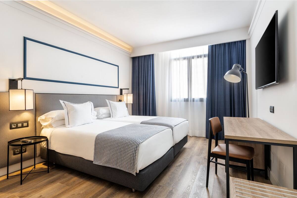 Et hotelværelse med en stor seng, et skrivebord og et fjernsyn.