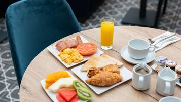 A breakfast table with plates of eggs, toast, croissants, and fruit, a glass of orange juice, and coffee cups.