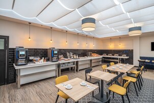 Un restaurante moderno con una barra alargada, varias mesas y sillas. Hay luces colgantes y un techo de diseño único.