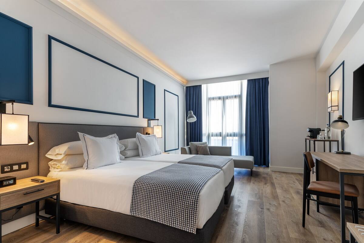 Et hotelværelse med en stor seng, sengeborde, et skrivebord og en stol.