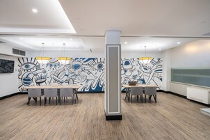Una sala de conferencias moderna con dos mesas, sillas y un gran mural abstracto en la pared.