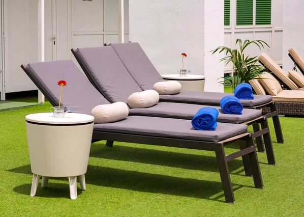 A set of lounge chairs with cushions, a small table with a vase of flowers, and a potted plant.