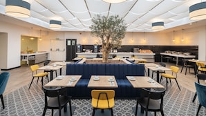 A modern restaurant with a central seating area, multiple dining tables, and a large tree in the middle. - Hotel LIVVO Fataga (Las Palmas de Gran Canaria)
