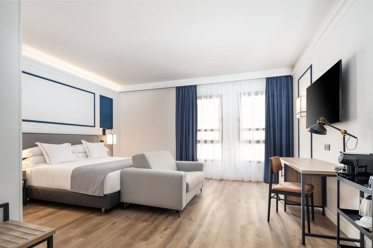 Et moderne hotelværelse med seng, sofa, skrivebord og fjernsyn.