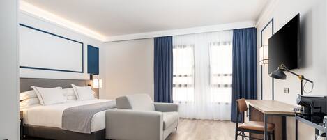 Een moderne hotelkamer met een bed, een sofa, een bureau en een televisie.