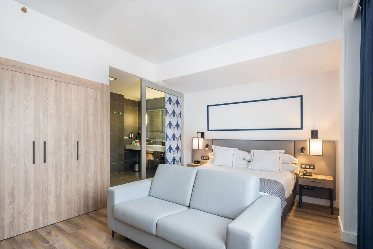 Et moderne hotelværelse med seng, sengeborde, en sofa og et garderobeskab.
