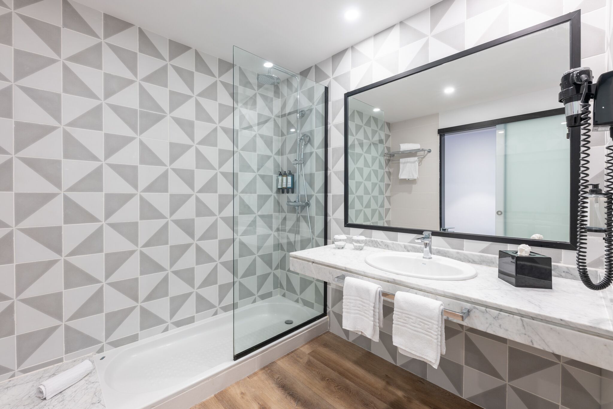 Une salle de bain moderne avec une douche à parois de verre, un grand miroir et un lavabo en marbre.