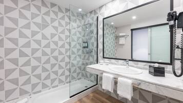 Un baño moderno con ducha de vidrio, un espejo grande y un lavamanos de mármol.