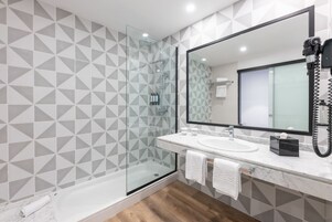 Un baño moderno con ducha de vidrio, un espejo grande y un lavamanos de mármol.