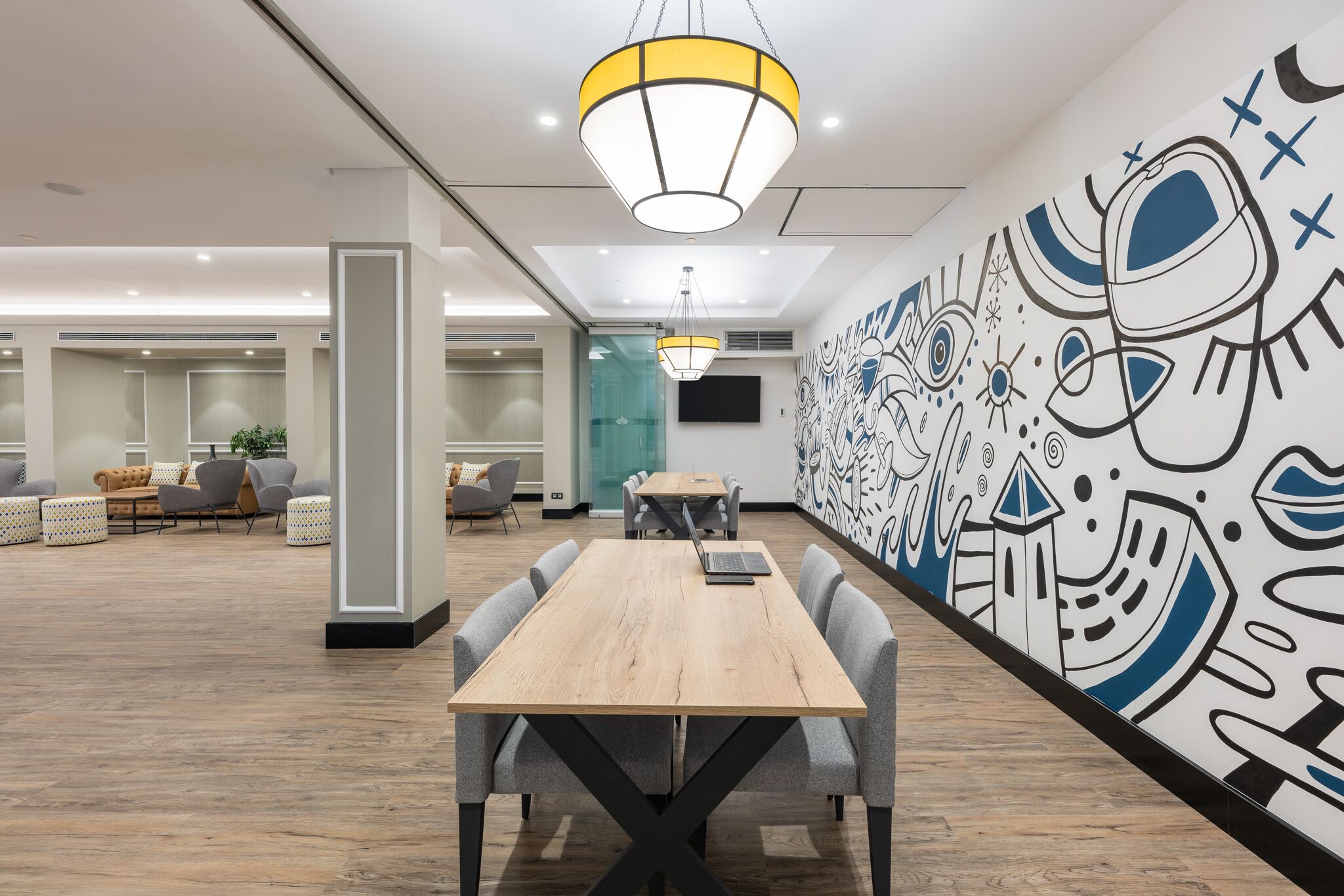 A modern office space with a long wooden table, grey chairs, and a colorful mural on the wall.