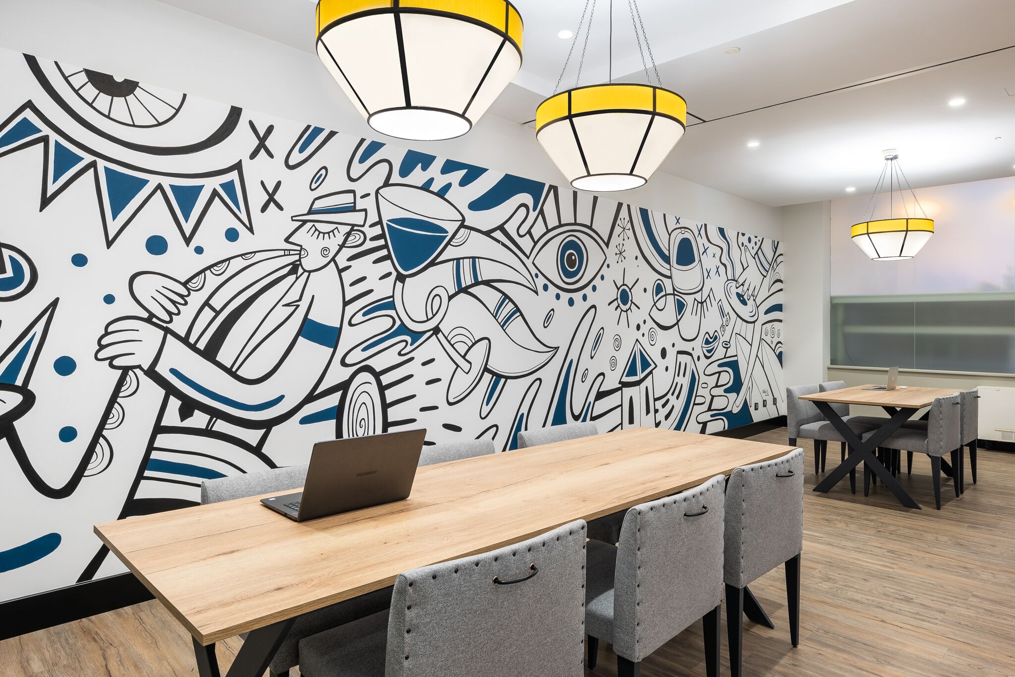 Un espacio de oficina moderno con un mural, mesas de madera y sillas grises.