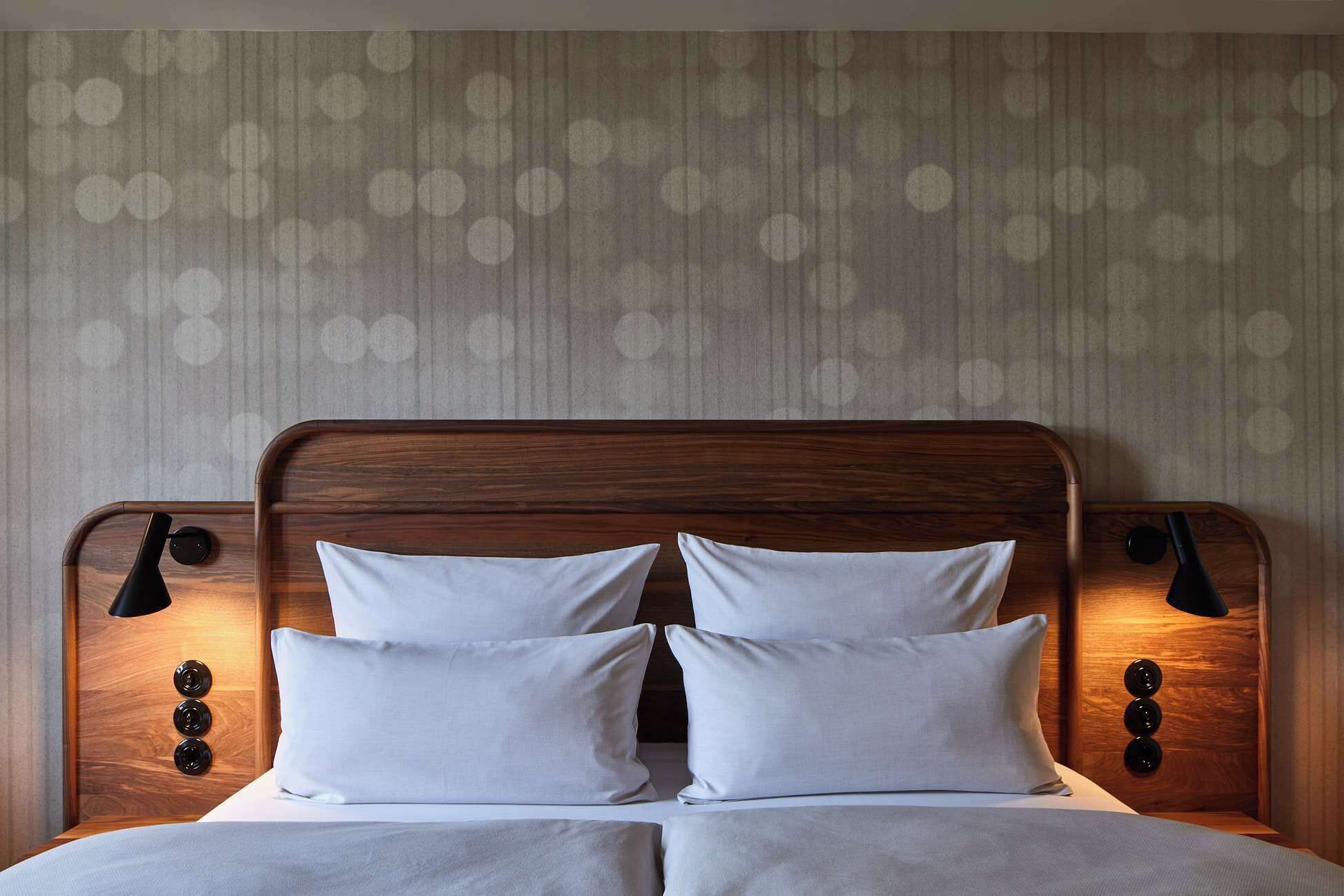 A bed with a wooden headboard, two white pillows, and a light-colored bedspread.