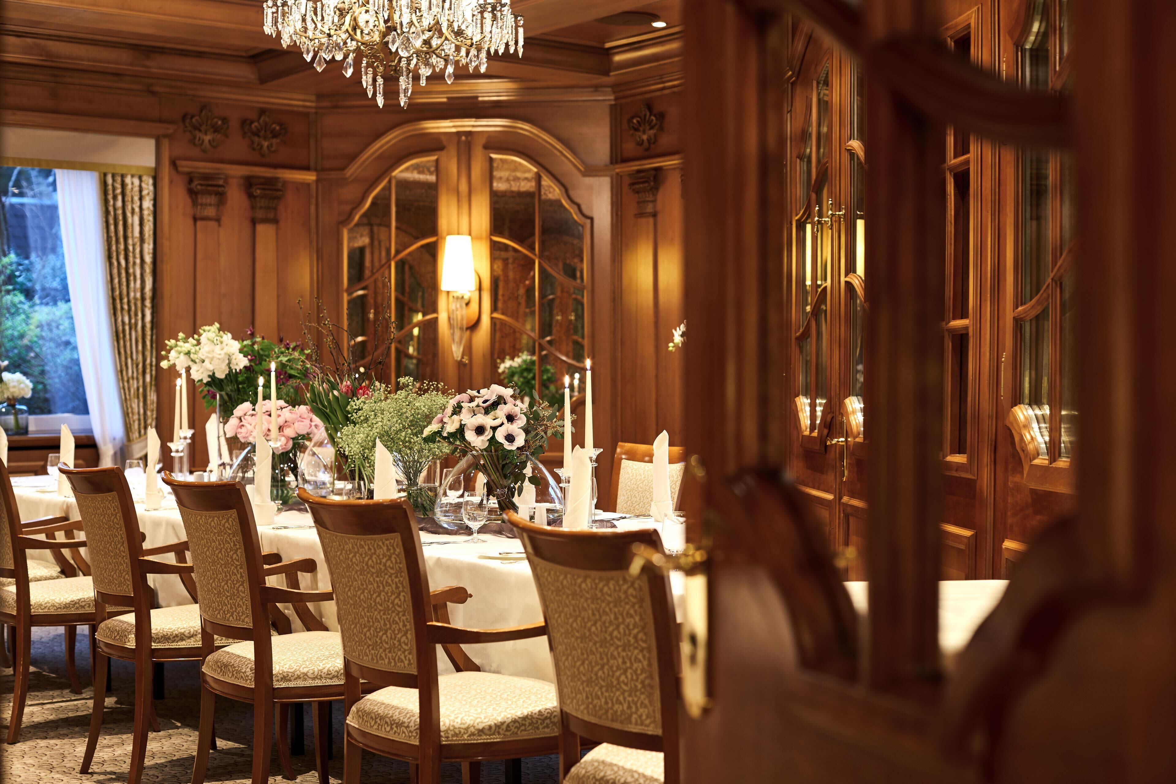 A formal dining room with a chandelier, wooden paneling, and a large window with curtains.