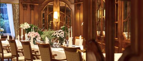A formal dining room with a chandelier, wooden paneling, and a large window with curtains.