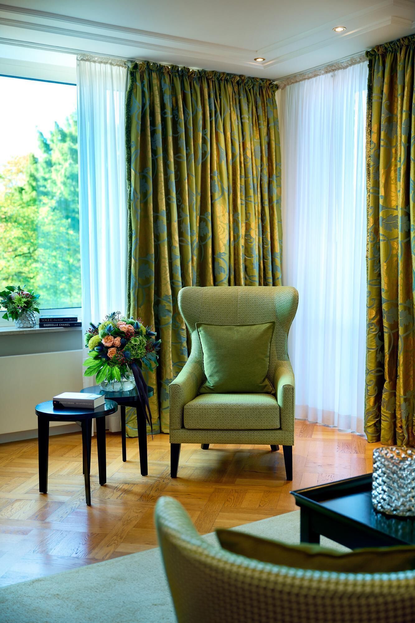 Um quarto com uma poltrona estampada, uma mesinha com um vaso de flores e cortinas com motivos florais.