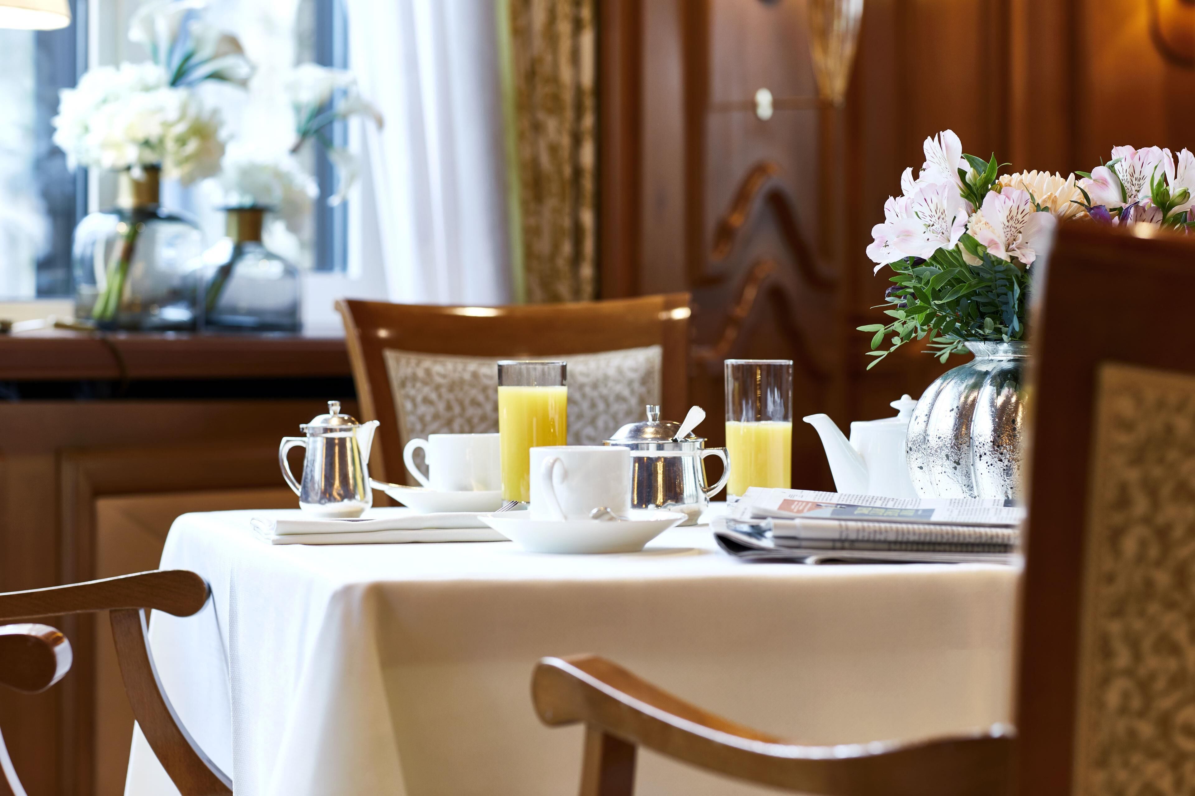 A breakfast setting with a table set for two, including a pitcher of orange juice, a teapot, and a vase of flowers.