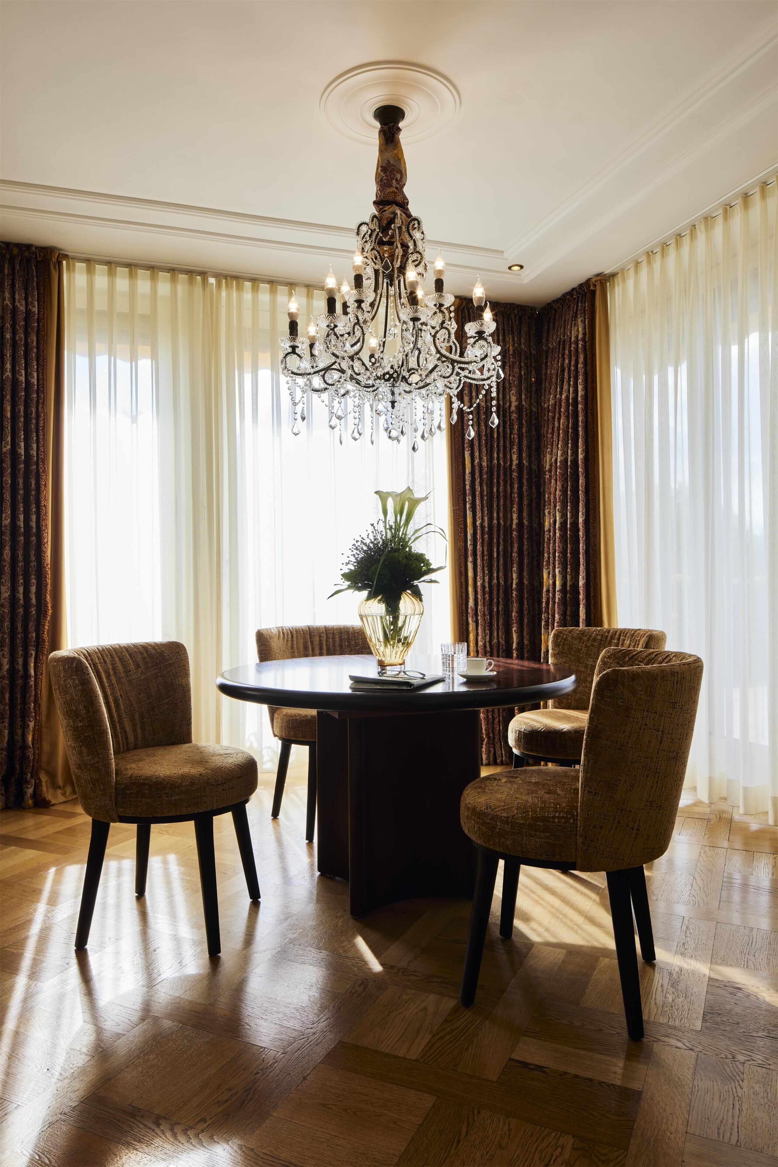 A dining area with a chandelier, a round table, and four upholstered chairs.