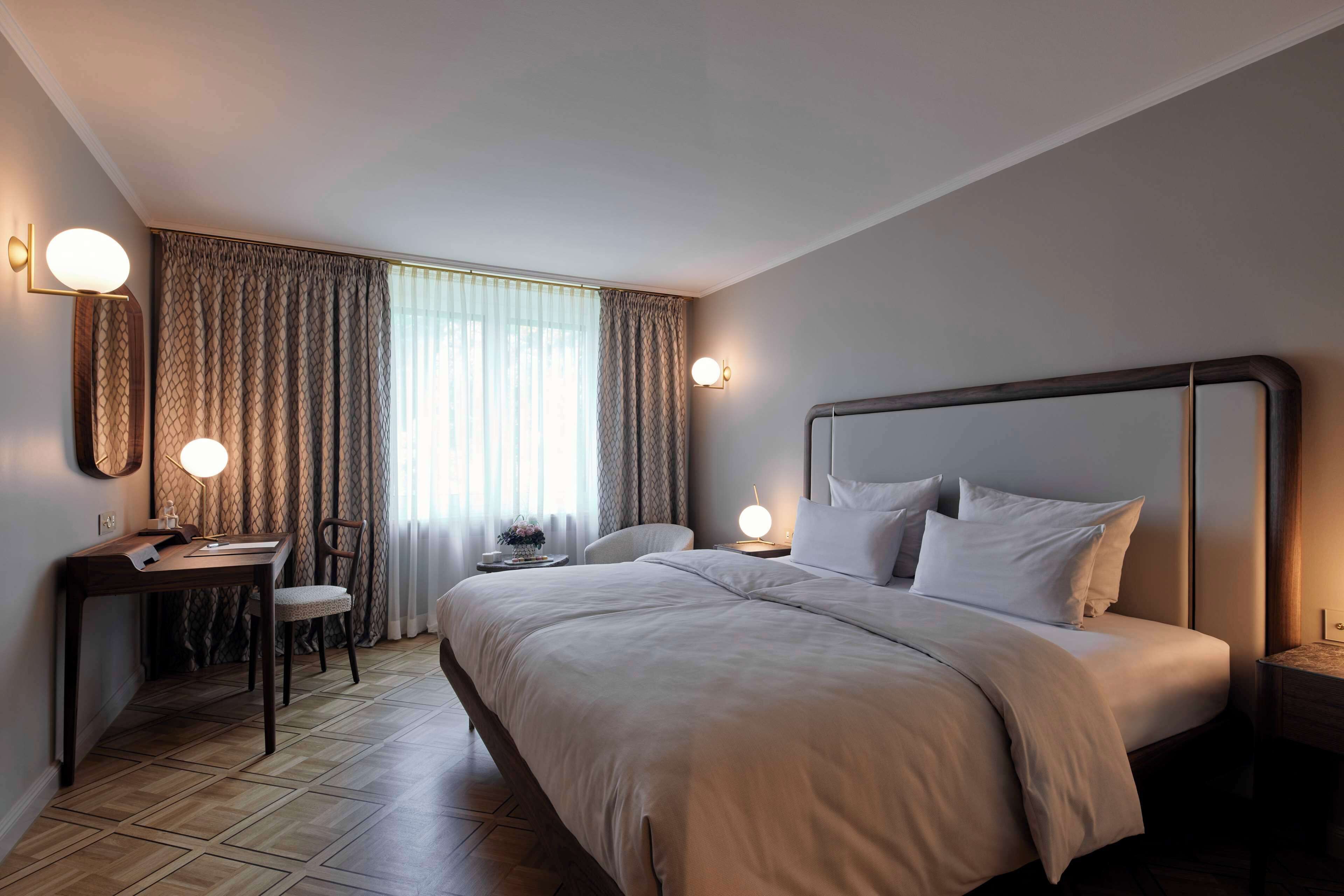 Et hotelværelse med en stor seng, et skrivebord, en stol og et natbord med en lampe.