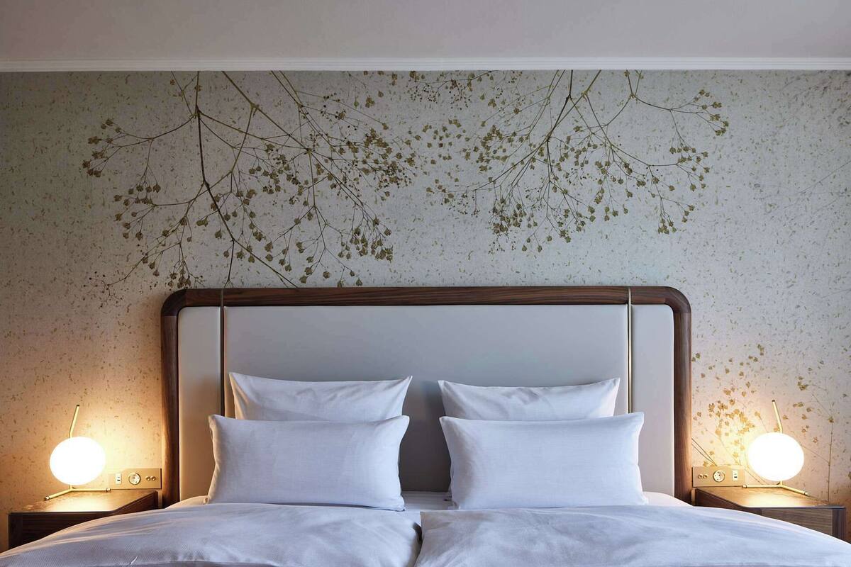 Ein Hotelzimmer mit einem großen Bett, zwei Nachttischen mit Lampen und einer Wand mit Blattmuster.