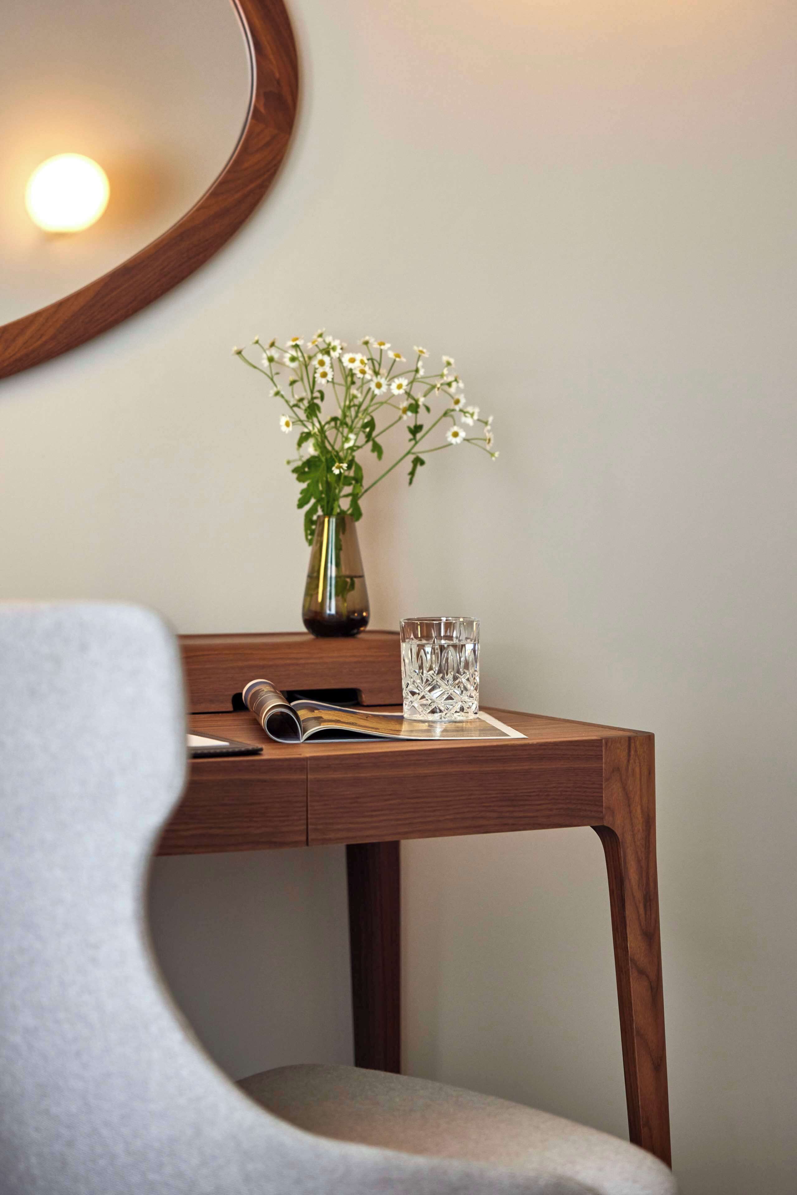 A wooden desk with a vase of flowers and a glass.