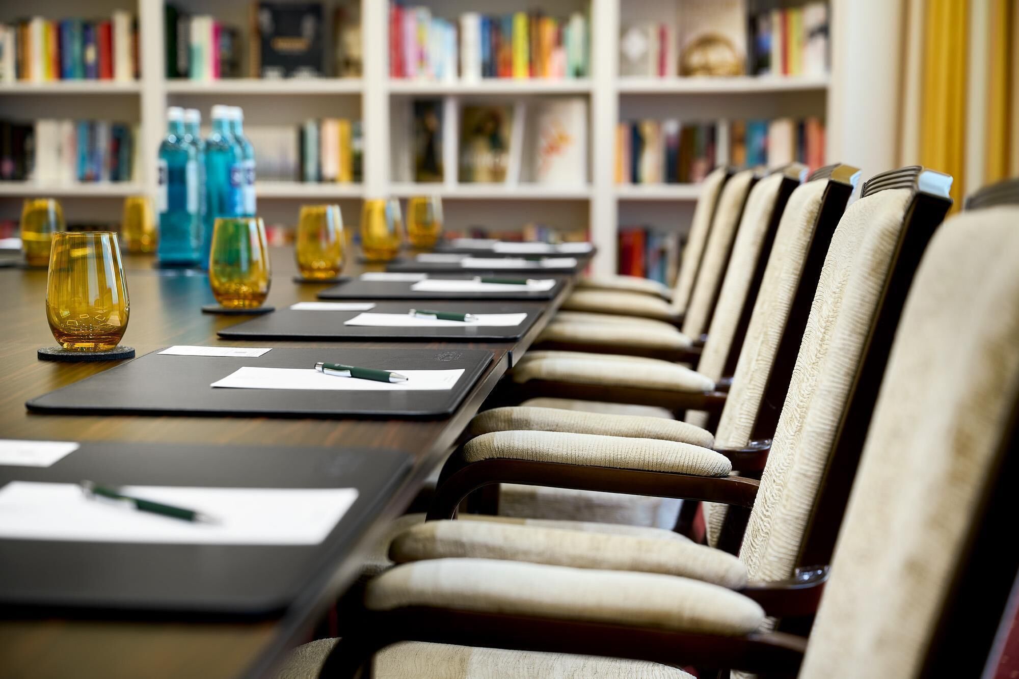 Una sala de conferencias con una larga mesa, sillas y una estantería al fondo.