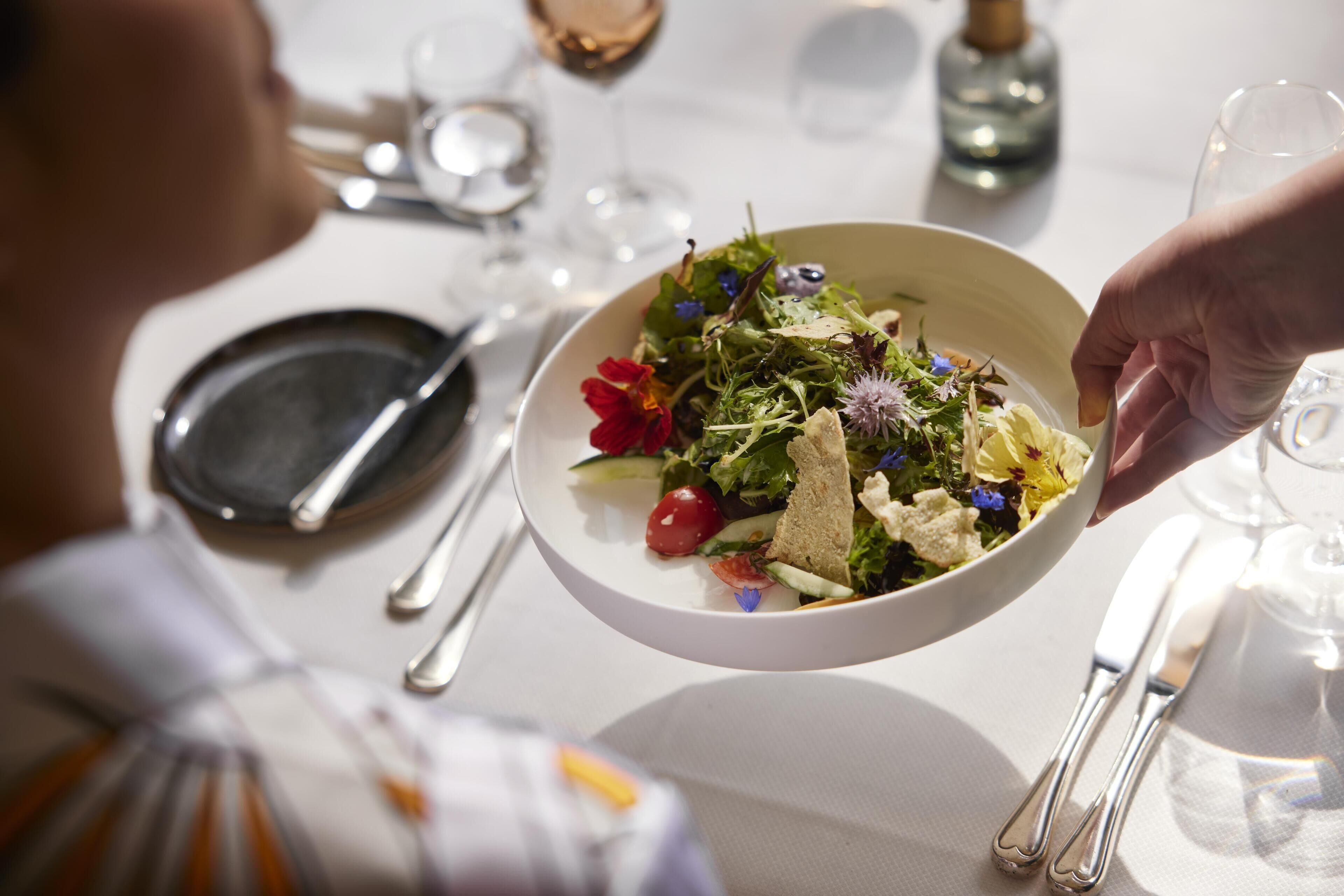 A dining table with a white tablecloth, a bowl of salad, and a wine glass.