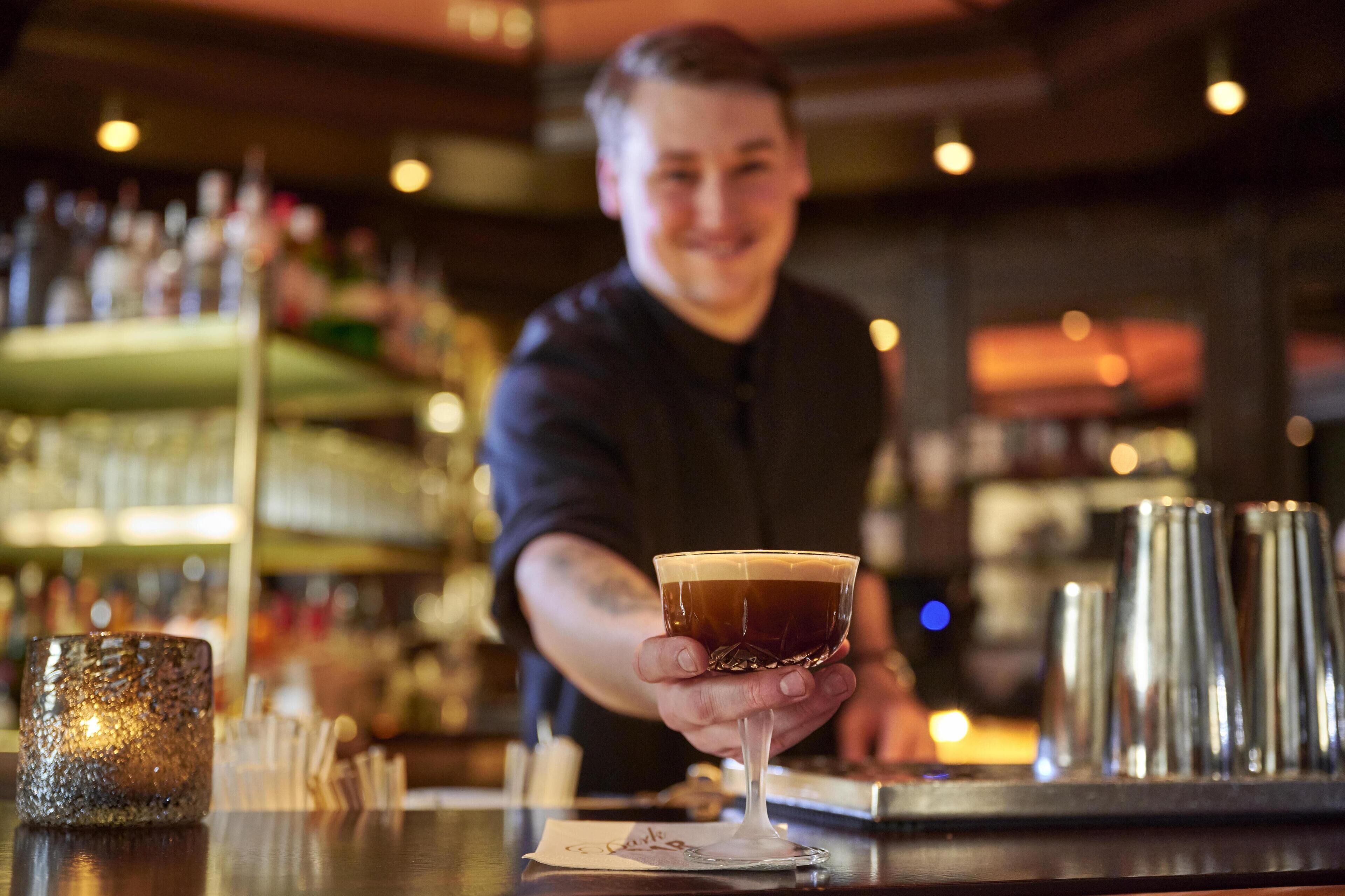 A bartender holding a cocktail glass at a bar.