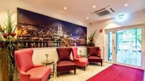 A hotel lobby with red chairs, a large cityscape mural, and a red carpet. - CityClass Hotel am Heumarkt (Cologne)