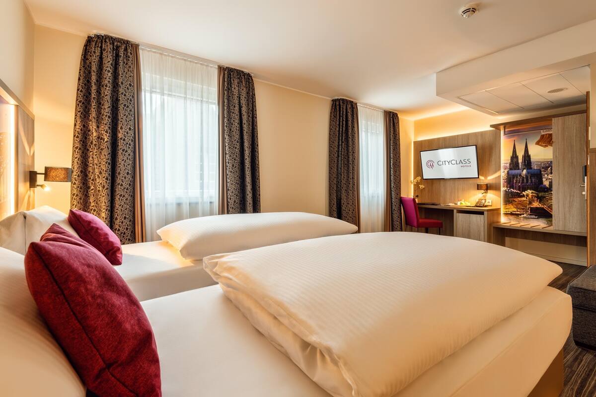 Habitación de hotel con dos camas, un escritorio, un televisor y un cartel con vistas a la ciudad.