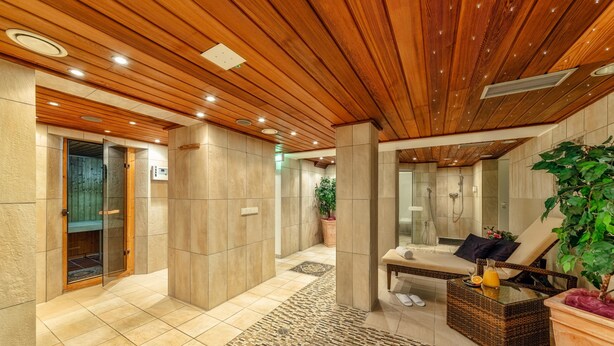 A modern spa area with a wooden ceiling, tiled floors, a massage table, a massage chair, and a large potted plant. - CityClass Hotel am Heumarkt (Cologne)