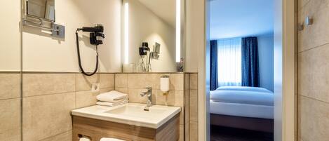 Un baño de hotel con lavamanos, espejo, secador de pelo y toallero.