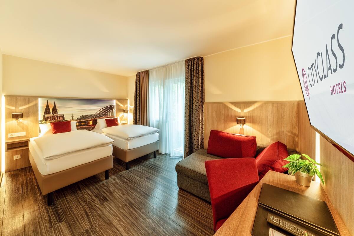 Habitación de hotel con dos camas, un sofá, un televisor y una pintura de un paisaje urbano.