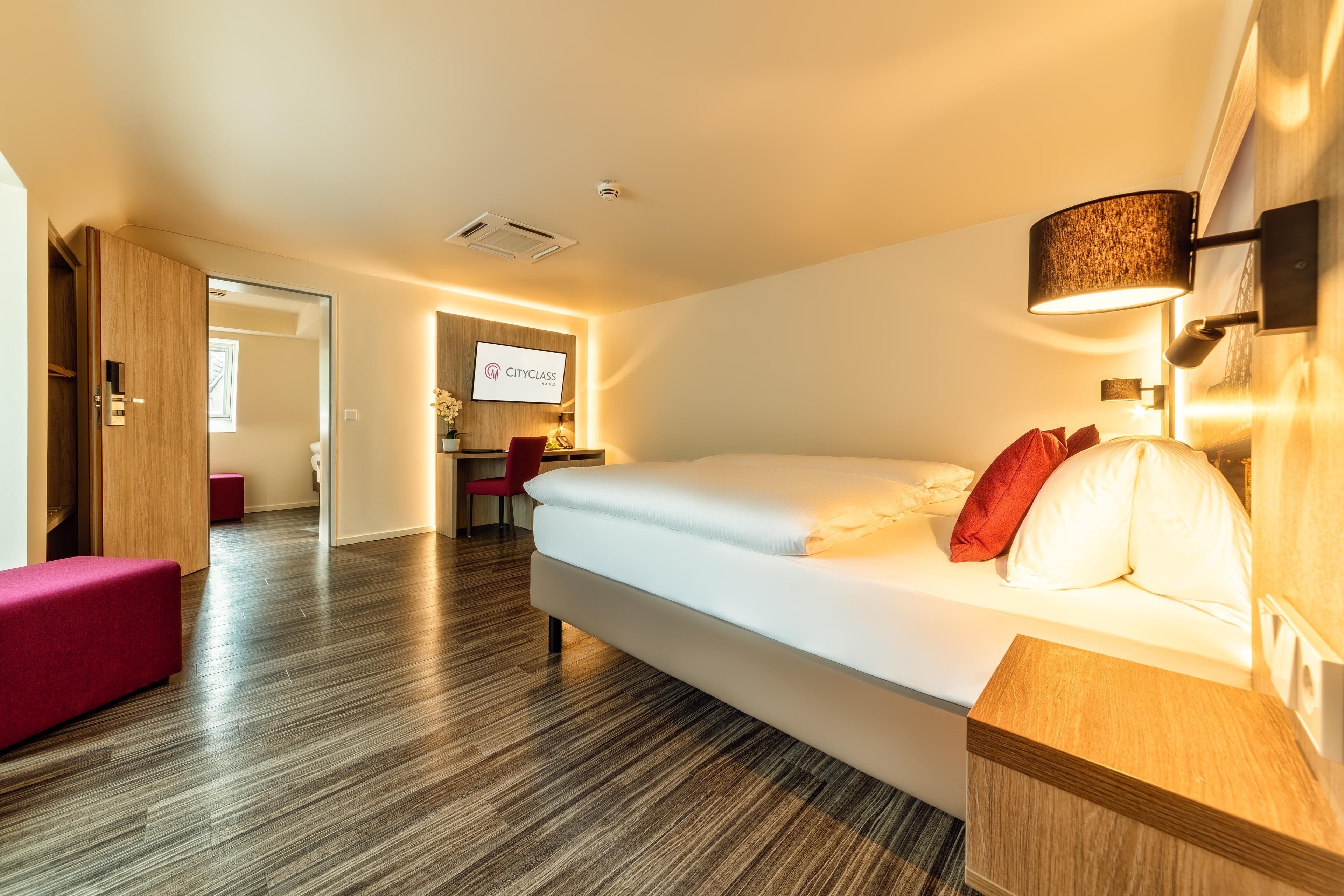 A hotel room with a bed, a desk, a chair, and a TV.