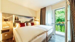 A hotel room with a large bed, a nightstand, a wall-mounted lamp, and a window with a view of greenery. - CityClass Hotel am Heumarkt (Cologne)