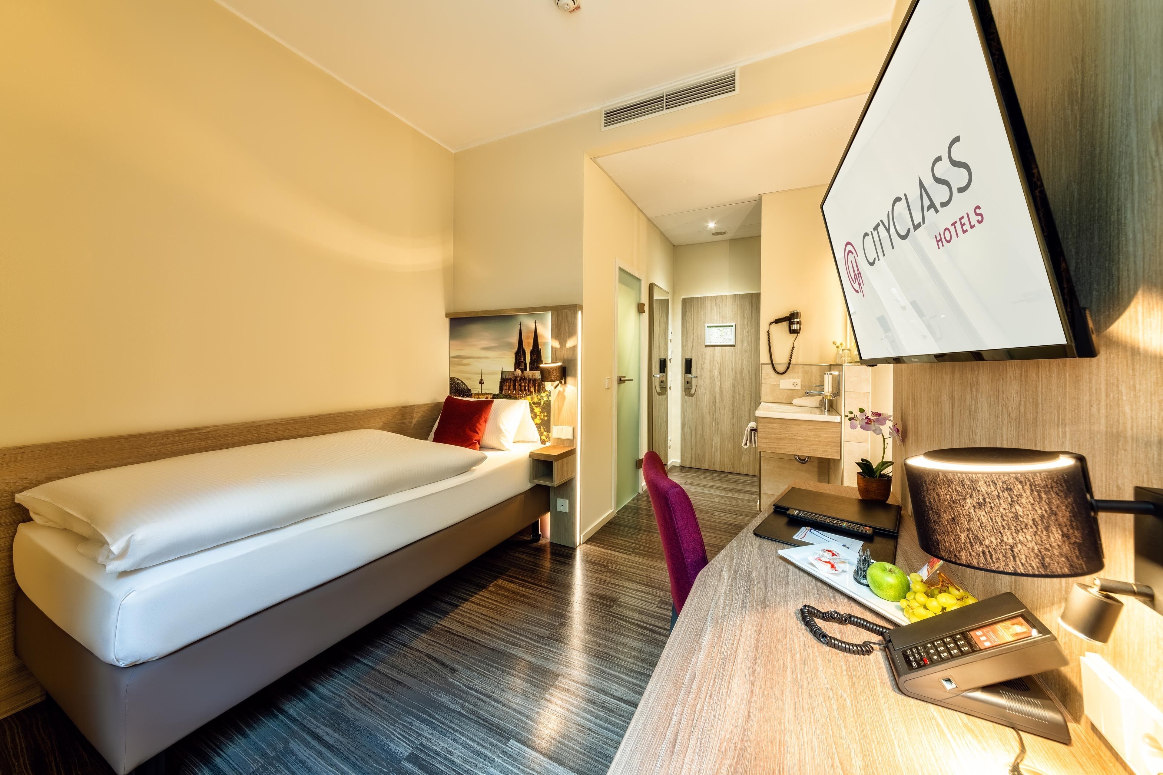 Een hotelkamer met een bed, bureau, stoel en een lijst met een bordje aan de muur.