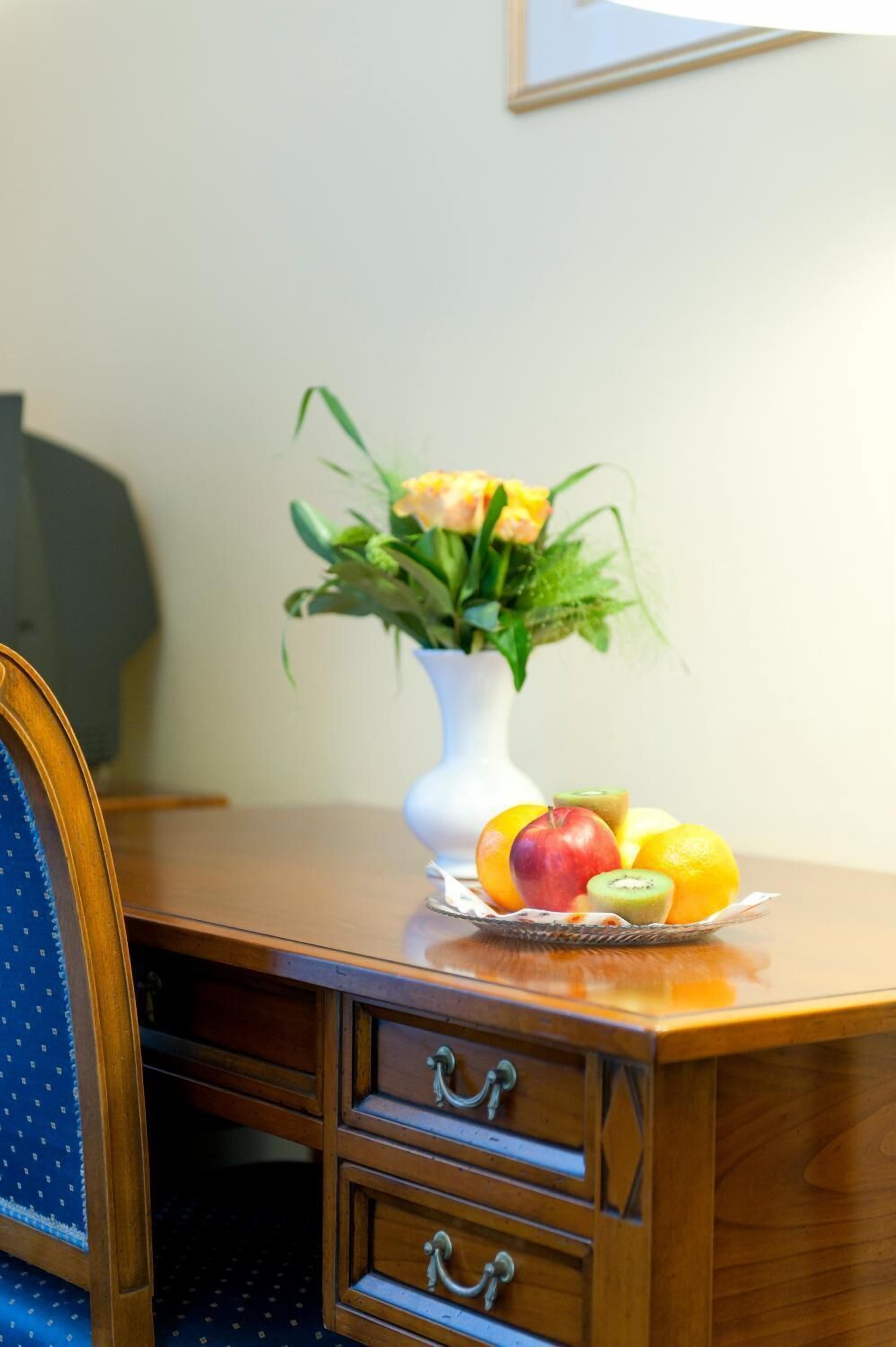 A wooden desk with a vase of flowers and a fruit bowl.