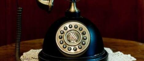 A vintage rotary dial telephone on a wooden table with a lace doily.