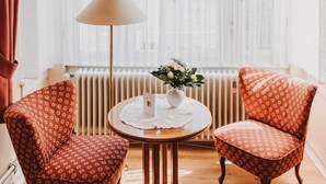 A room with two patterned armchairs, a round wooden table with a white lace tablecloth, a floor lamp, and a window with sheer curtains. - Hotel Spoettel (Bad Nauheim)