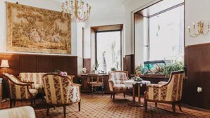 A room with patterned chairs, a chandelier, a large painting, and a view of the outdoors. - Hotel Spoettel (Bad Nauheim)