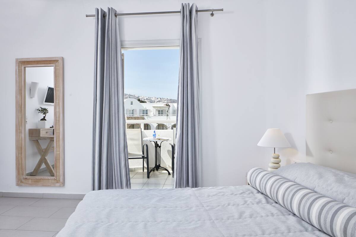Ein Hotelzimmer mit Bett, Nachttisch mit Lampe, Spiegel und Blick auf den Balkon.