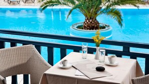 Una mesa junto a la piscina con mantel blanco, un jarrón con flores amarillas y un vaso de agua.