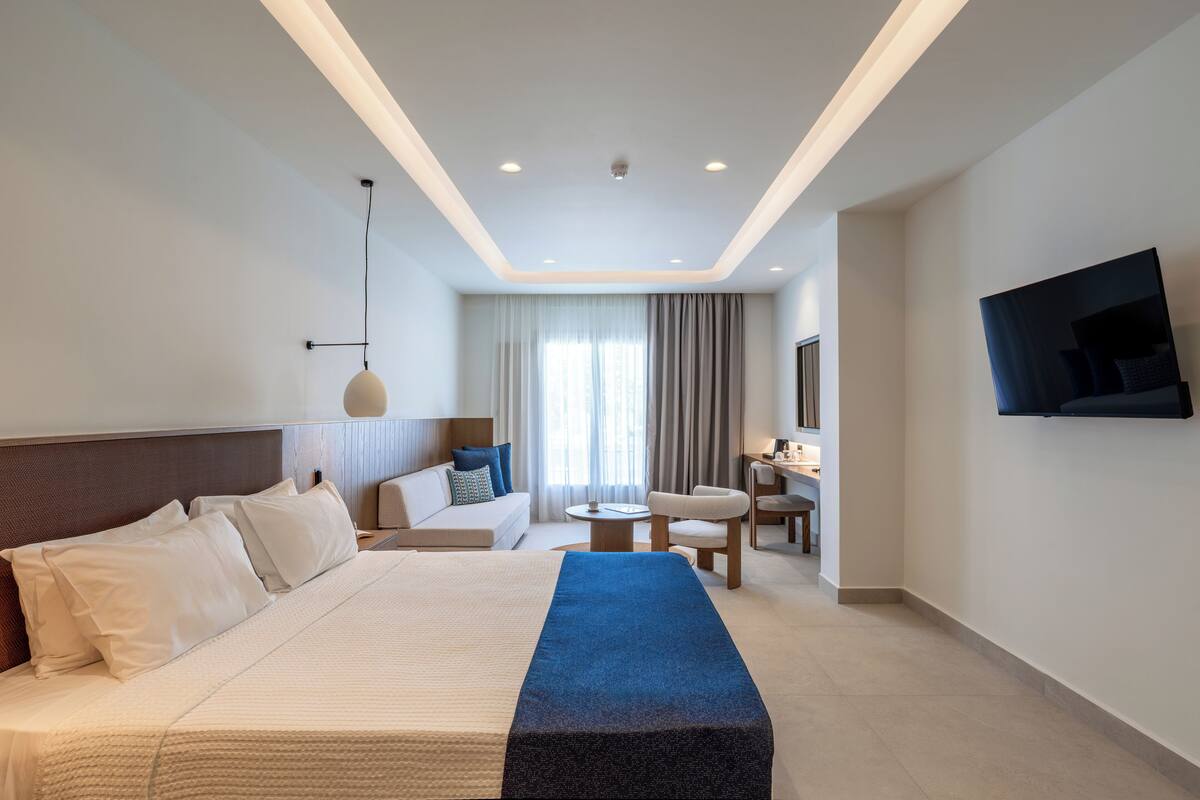 Ein modernes Hotelzimmer mit einem großen Bett, einer Couch, einem Schreibtisch und einem Fernseher.