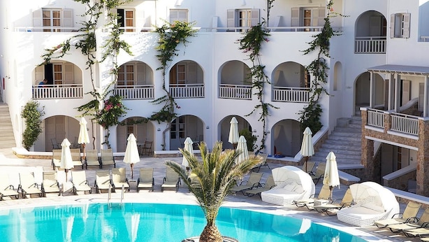 Un edificio blanco con varios balcones, piscina y mobiliario para exteriores.